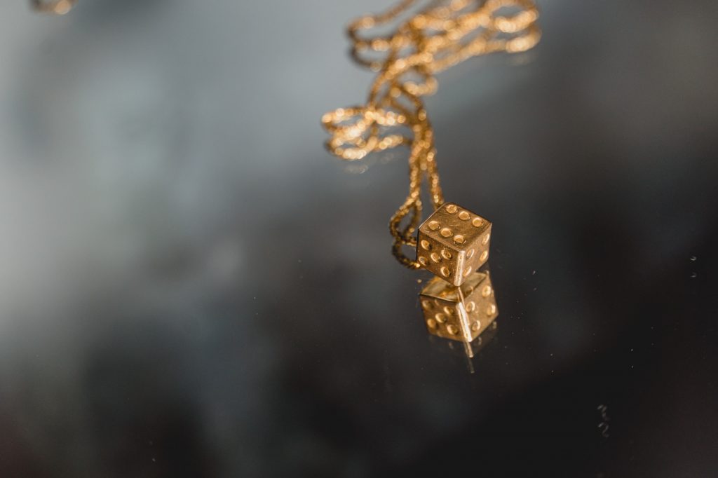 Dato Sri Darren Yaw's golden neckless focused on a dice with 6 tallies mirrored on a mirror grey background landscape